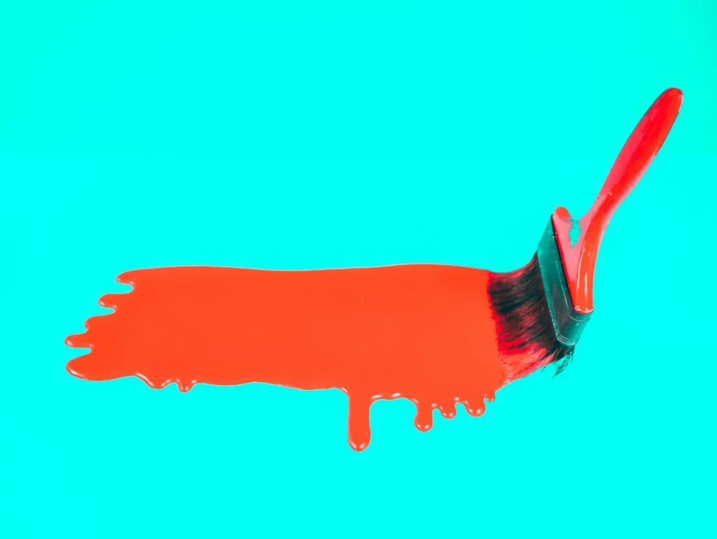 Paintbrush and orange paint on a cyan background