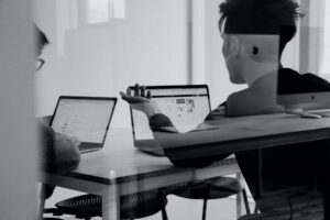 2 people in a glass office looking at laptops