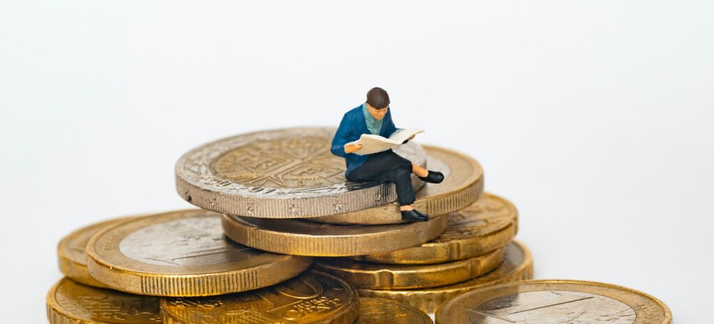 Small figurine of a man reading a newspaper atop a pile of coins