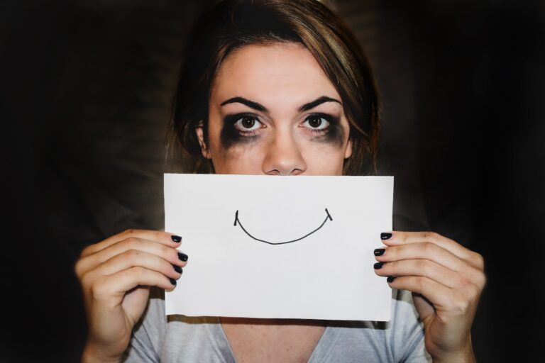 Lady with smudged mascara holding up a drawn smile in front of her mouth