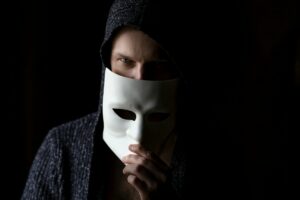 Hooded man pulling a white mask over his face.