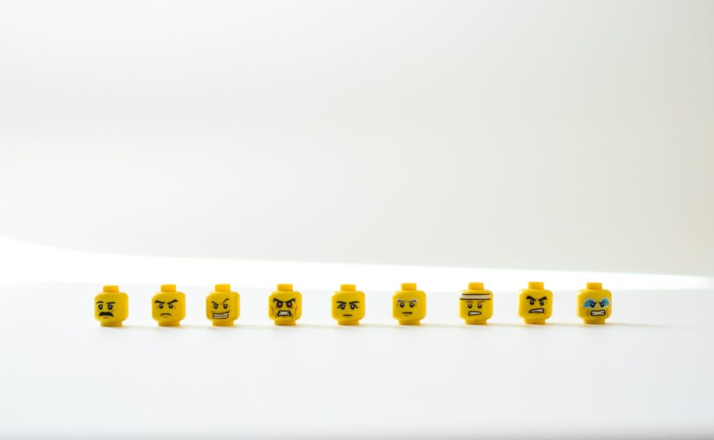 A row of LEGO heads on a white table. The faces show a range of negative emotions .