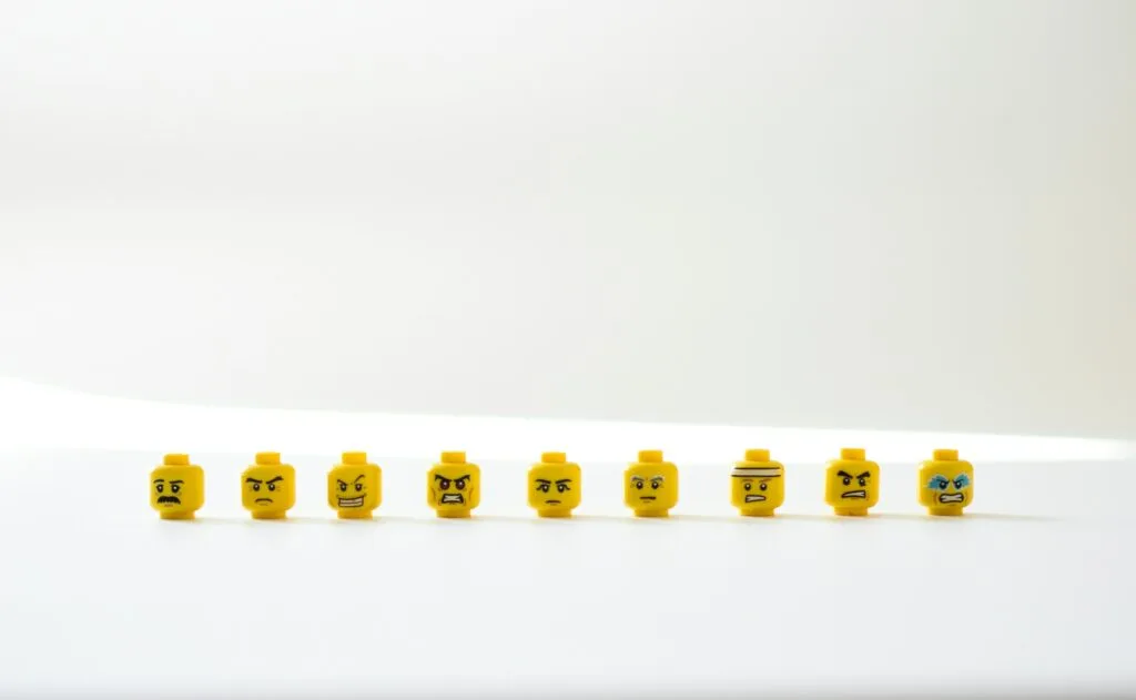 A row of LEGO heads on a white table. The faces show a range of negative emotions .