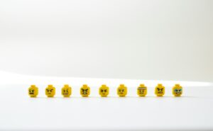 A row of LEGO heads on a white table. The faces show a range of negative emotions .