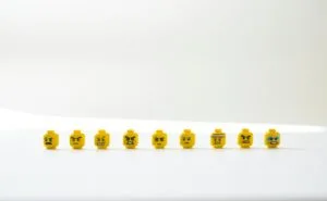 A row of LEGO heads on a white table. The faces show a range of negative emotions .