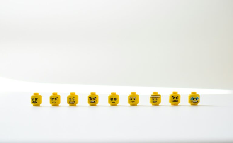 A row of LEGO heads on a white table. The faces show a range of negative emotions .