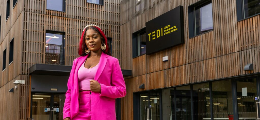 Generation Z female worker in a bright pink suit. She is standing outside teh Engineering and Design Institute building in London.