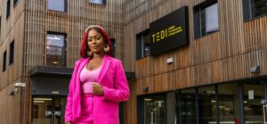 Generation Z female worker in a bright pink suit. She is standing outside teh Engineering and Design Institute building in London.