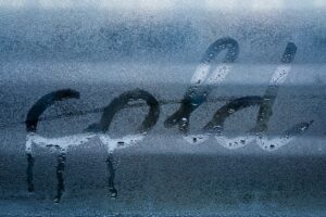 Condensation streaks down a window pane. The word "cold" is written in the condensation, highlighting the temperature difference causing the water droplets.