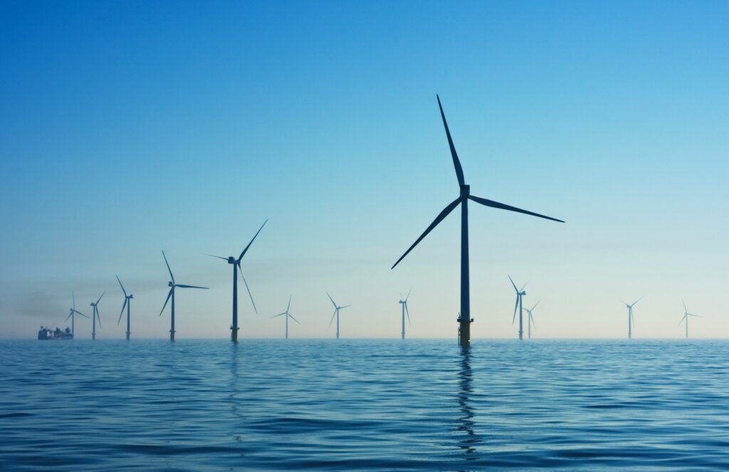 Several wind turbines stand in the sea under a clear blue sky in the UK.