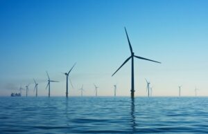 Several wind turbines stand in the sea under a clear blue sky in the UK.