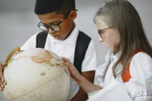 Two young students, a boy and a girl, closely examining and discussing a large globe together. They both appear intently focused on the world map, suggesting an educational and collaborative learning experience.