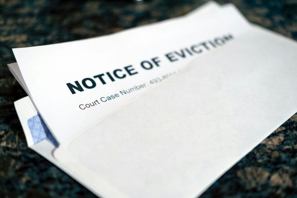 A close-up photograph of a legal document titled "NOTICE OF EVICTION" with a court case number visible below the title. The document appears to be a white paper lying on a dark-colored textured surface, with the corner of another document or envelope visible underneath.