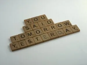 Wooden Scrabble tiles arranged to spell out "YOU SAID TOMORROW YESTERDAY" against a light background, conveying a message about procrastination and delays.